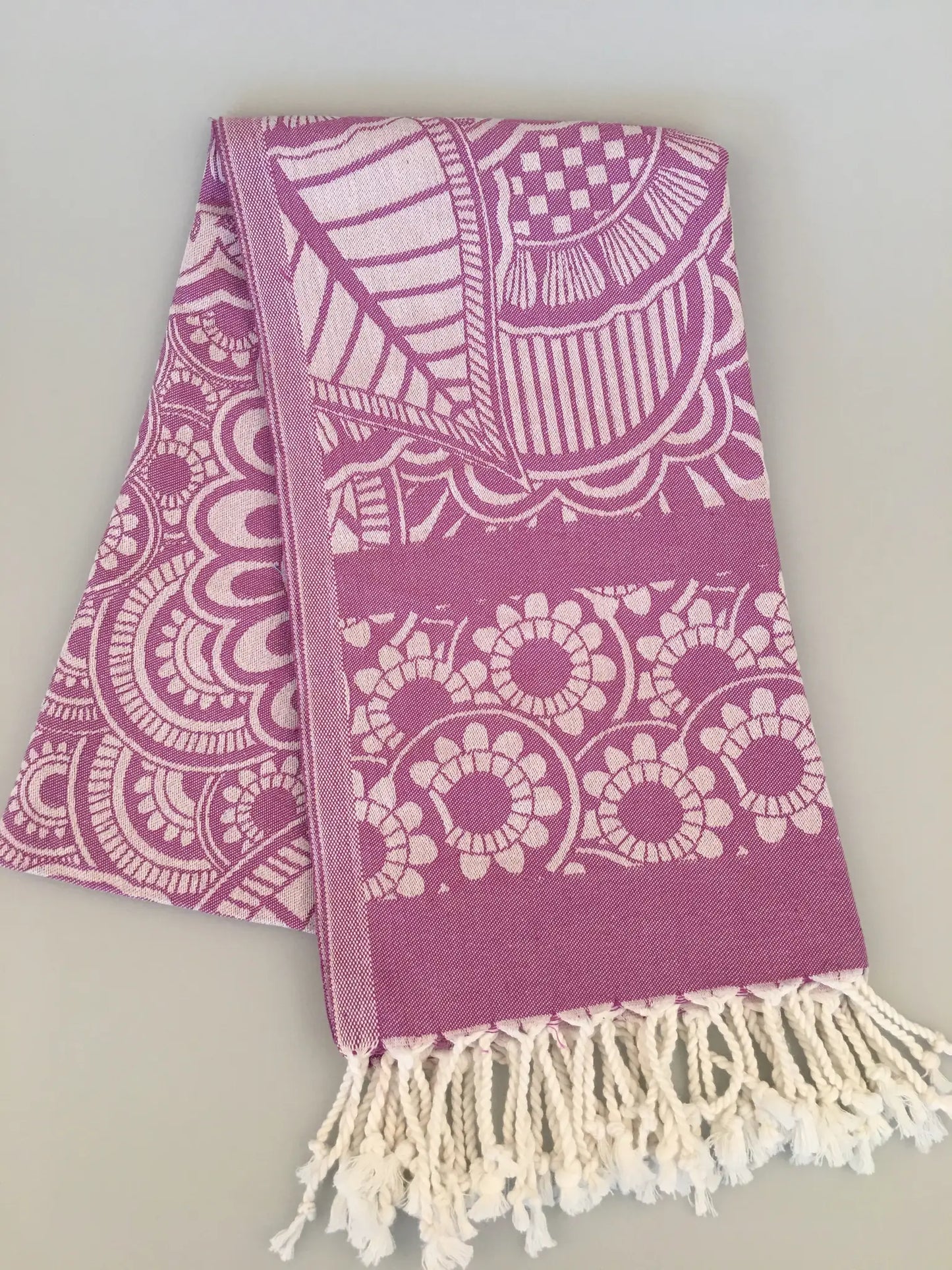 "Pink jacquard peshtemal towel with white intricate patterns and fringed edges, laid flat on a light background."