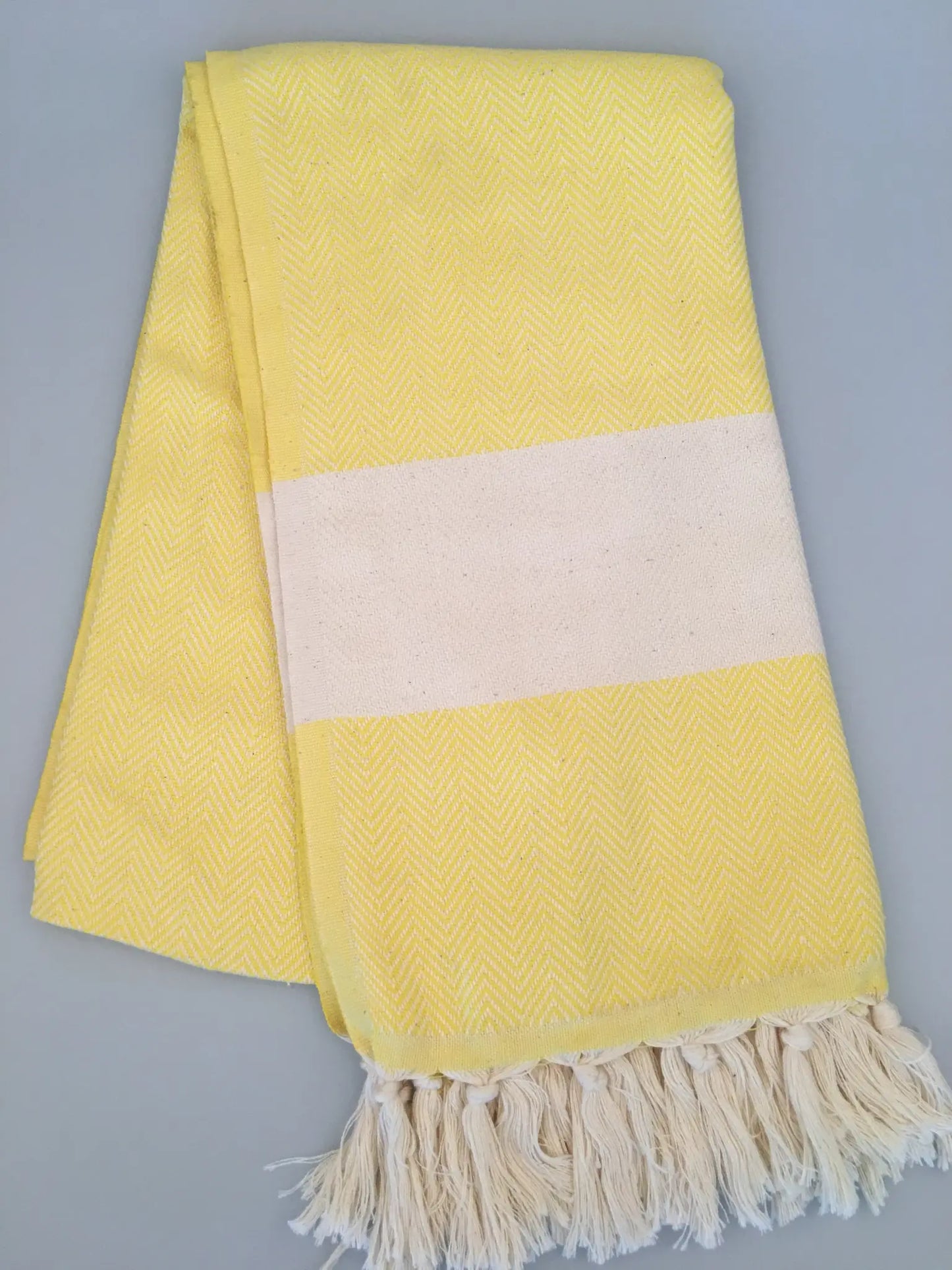 Yellow Turkish towel peshtemal with a white stripe and fringed edges, featuring a herringbone pattern.