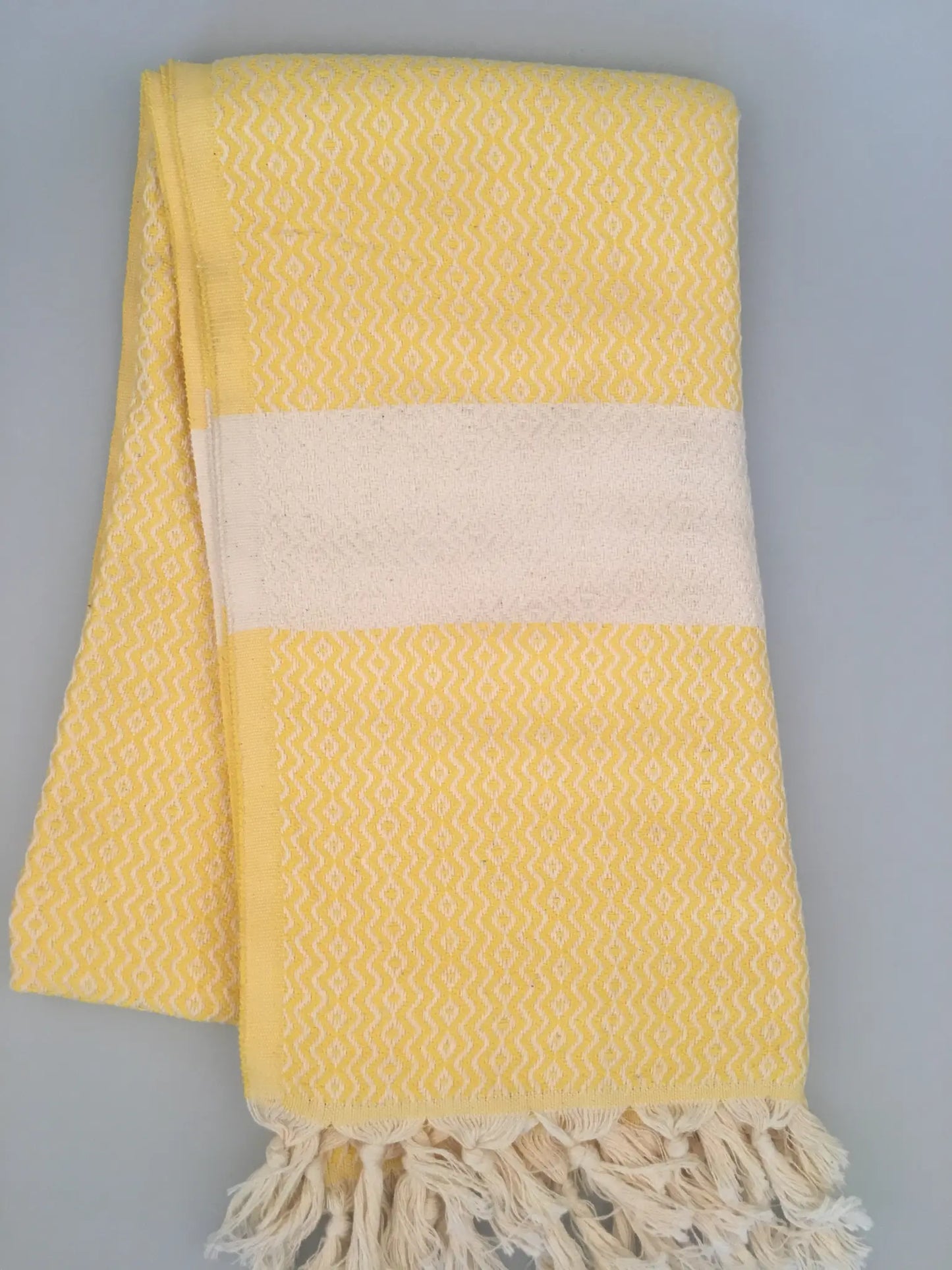 "Yellow Turkish towel with textured pattern and white stripe, folded with fringed edges."