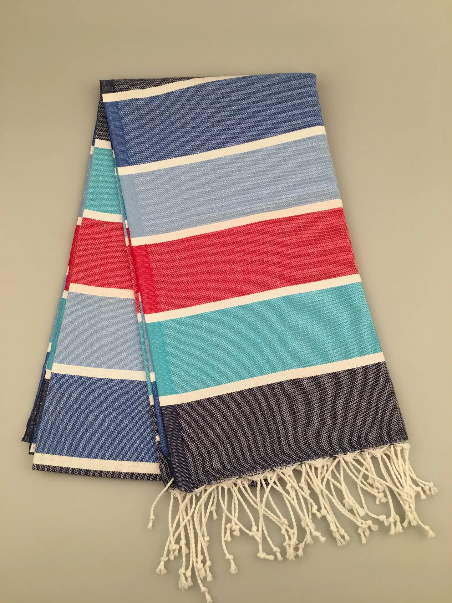 "Tripolis Turkish towel peshtemal with blue, teal, red, and white stripes, featuring fringed edges, laid flat."