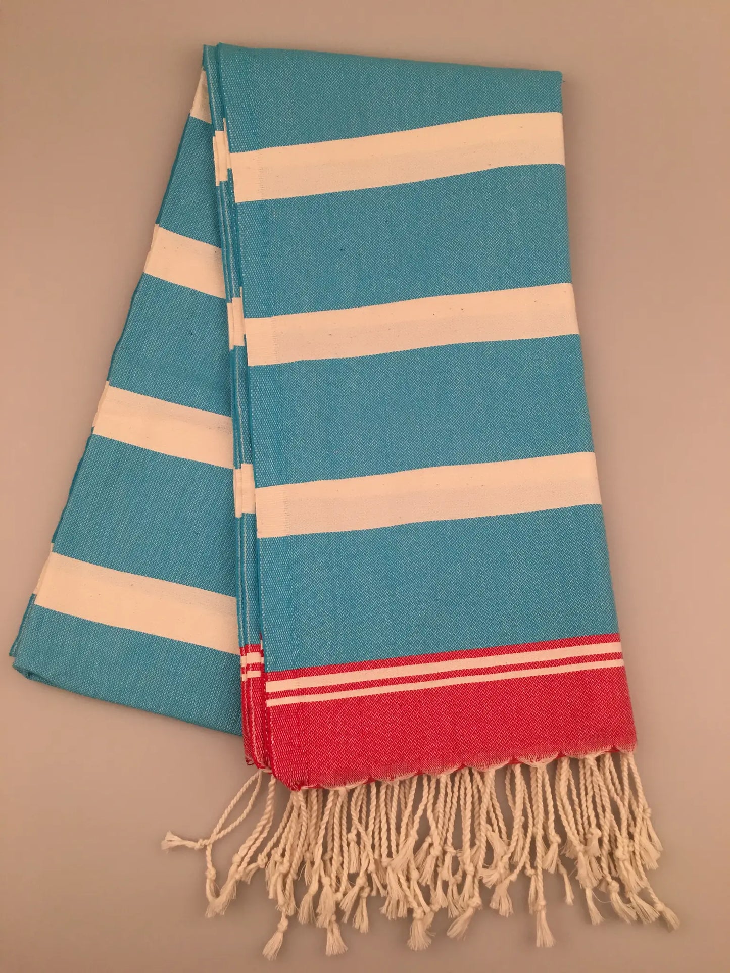 Turquoise and white striped Turkish towel with red accents and fringed edges, laid flat.