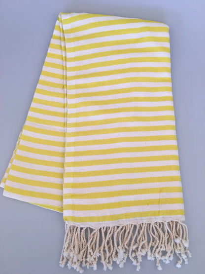 "Yellow and white striped Turkish towel with fringed edges, folded flat on a light gray background."
