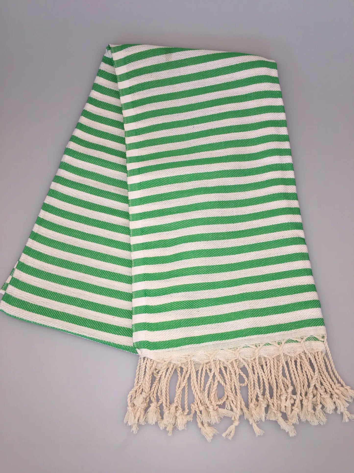 Green and white striped Turkish towel with fringed edges, folded neatly on a light gray background.