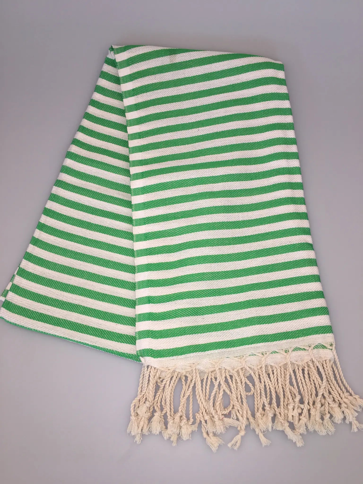 Green and white striped Turkish towel with fringed edges, folded neatly on a light gray background.
