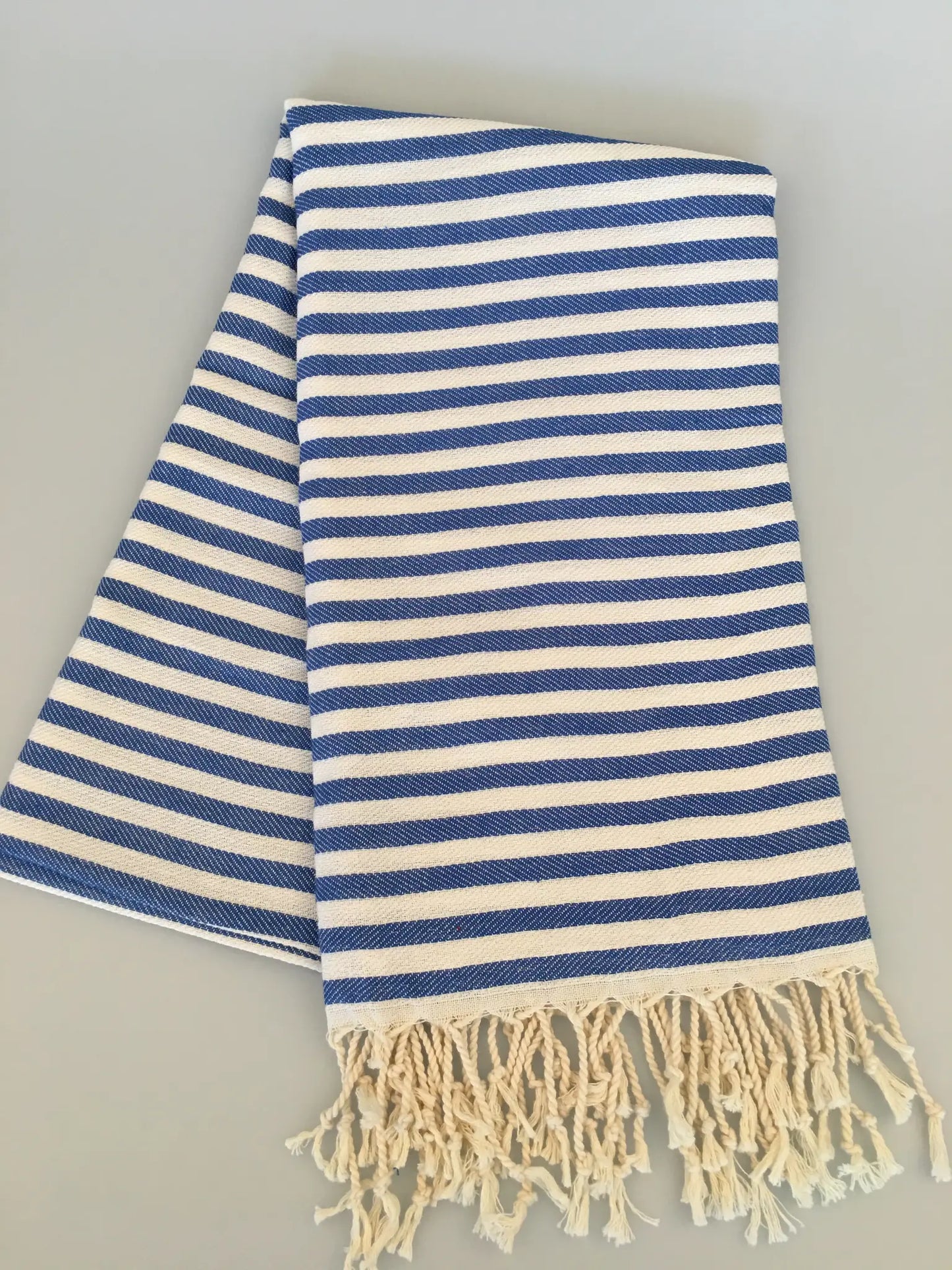 "Blue and white striped Turkish towel with fringed edges, neatly folded on a light background."