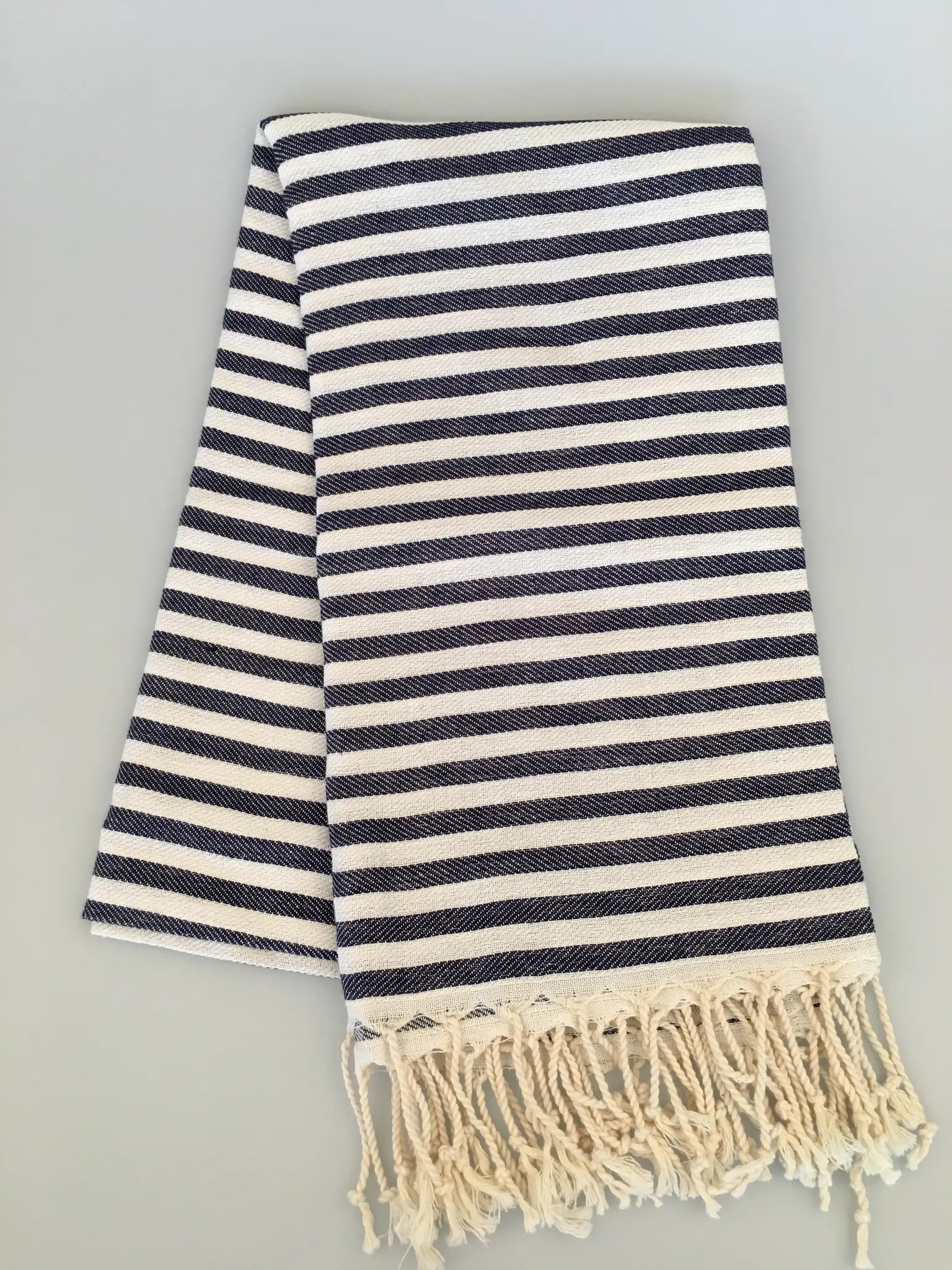 "Navy and cream striped Turkish towel with fringed edges, folded on a light gray background."