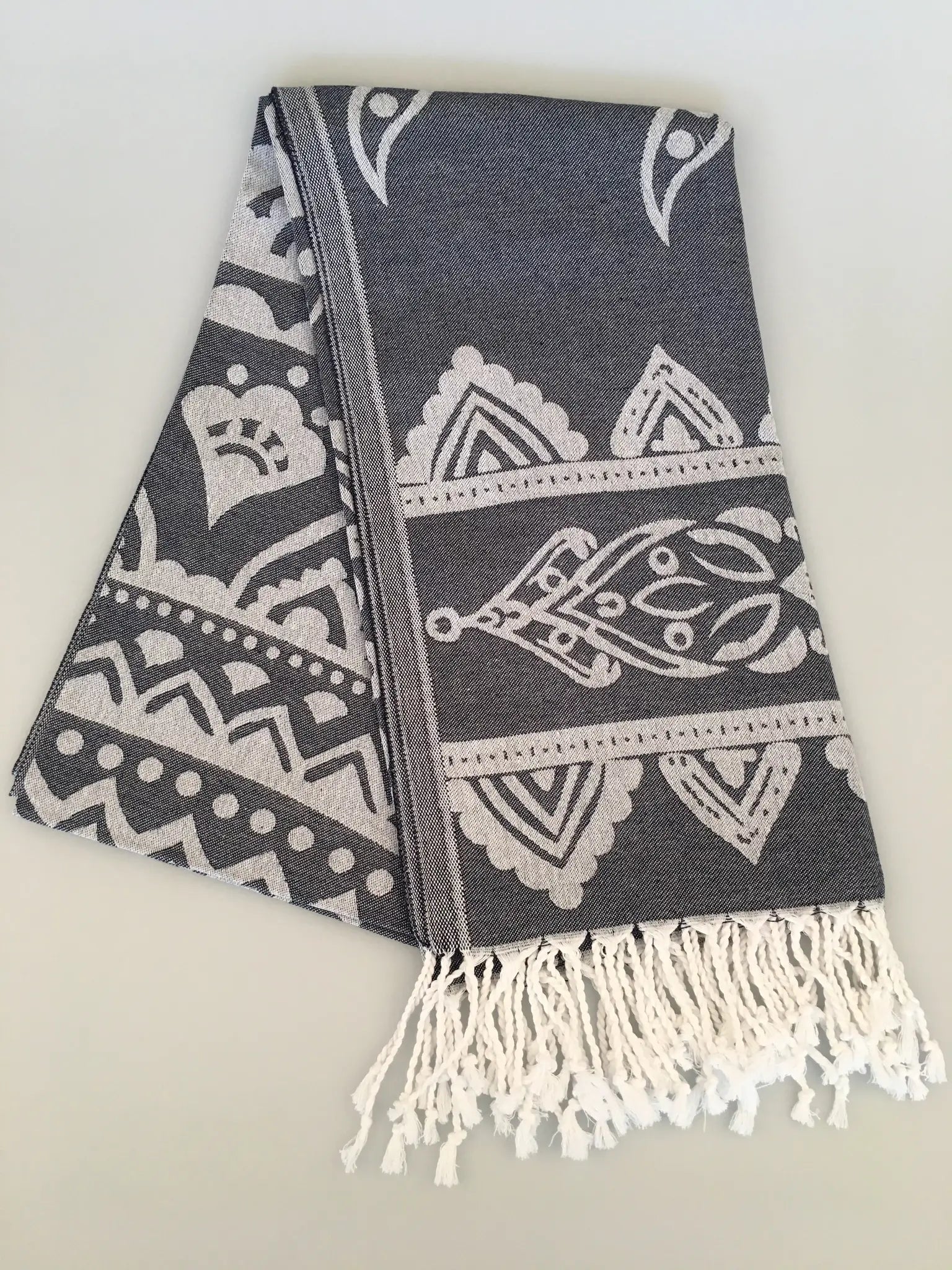 "Gray jacquard peshtemal towel with white intricate patterns and fringed edges, folded view on a light background."