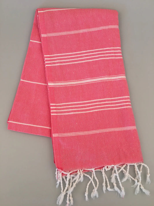 Coral pink Turkish towel with white stripes, fringed edges, and a lightweight, textured weave, laid flat.