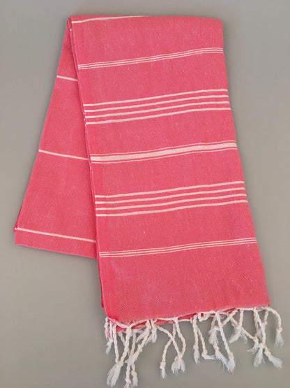 Coral Turkish towel with white stripes and fringed edges, folded on a neutral background.