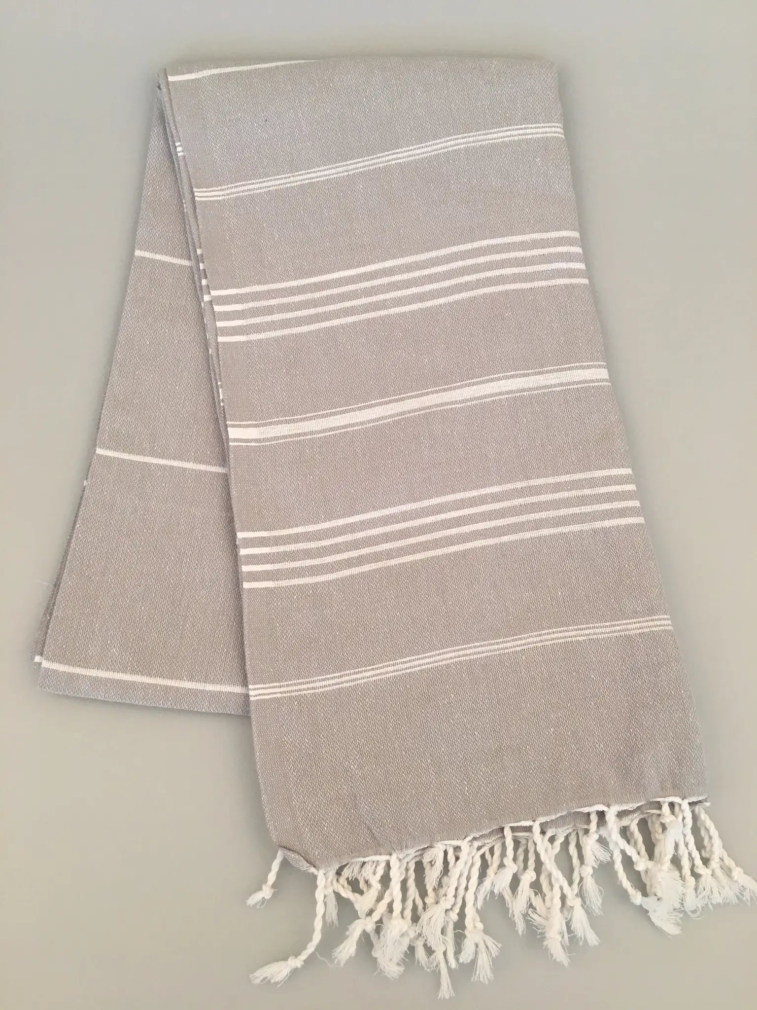 "Gray Turkish towel with white stripes and fringed edges, folded neatly on a light background."