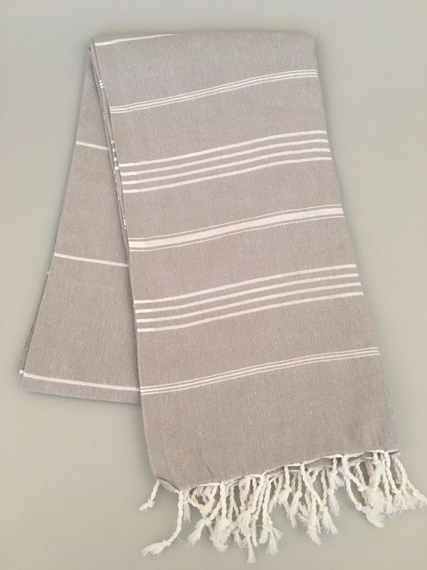 Light gray Turkish towel with white stripes and fringed edges, folded on a neutral background.
