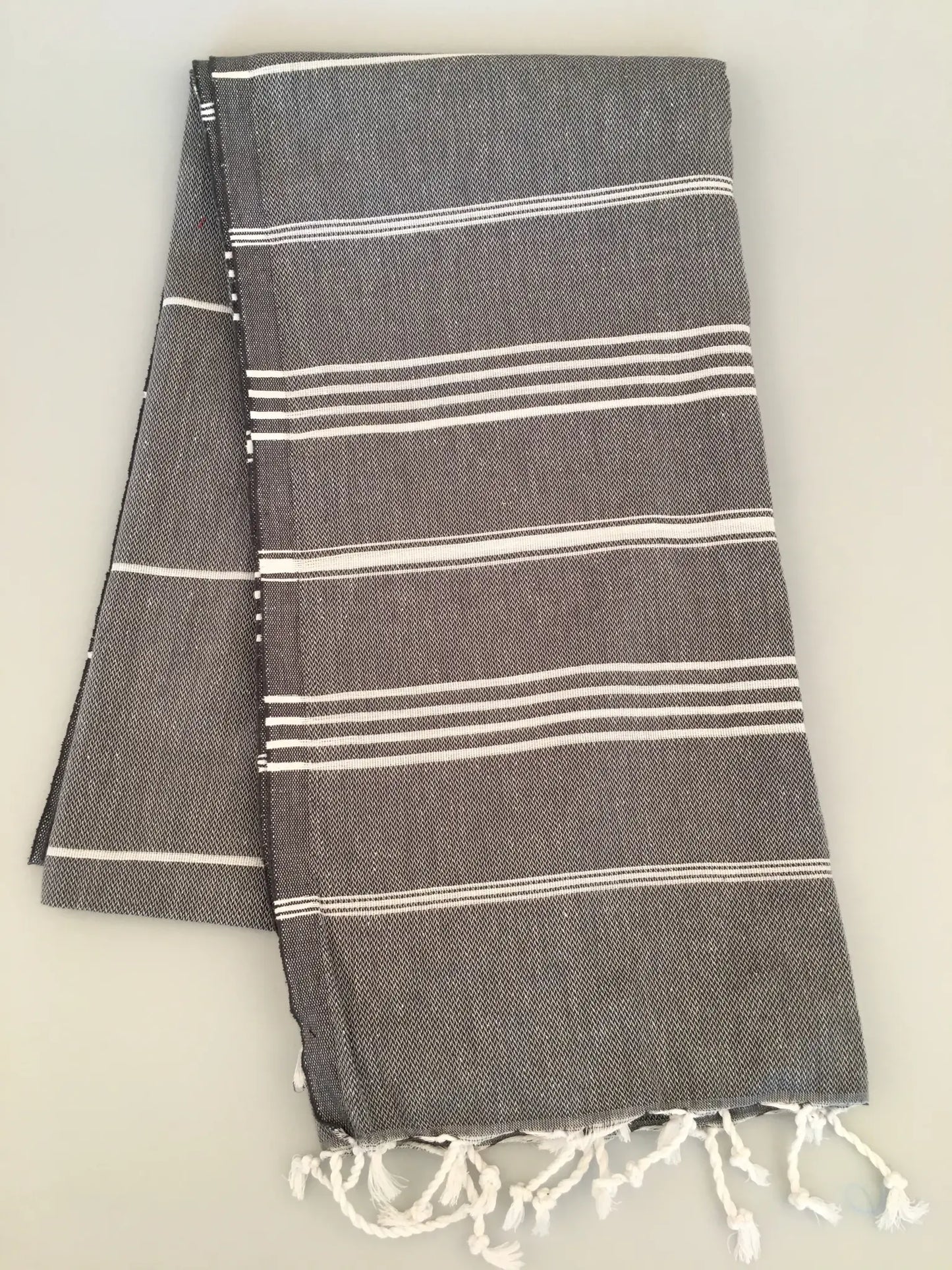 "Gray Turkish towel with white stripes and fringed edges, folded neatly on a light background."