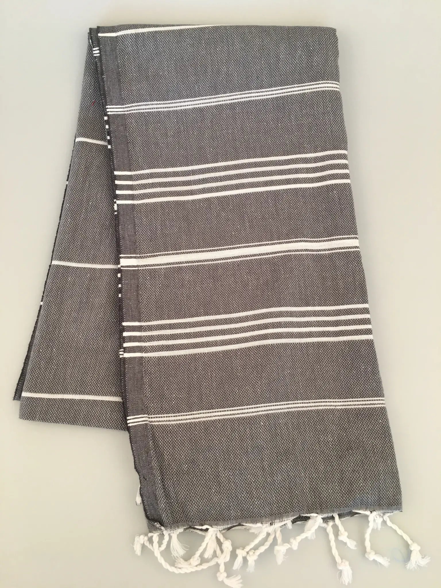 Gray Turkish towel with white stripes and fringed edges, folded neatly, showing soft texture and a lightweight design.