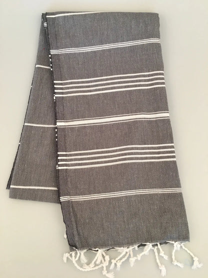 Gray Turkish towel with white stripes and fringed edges, folded neatly, showing soft texture and a lightweight design.