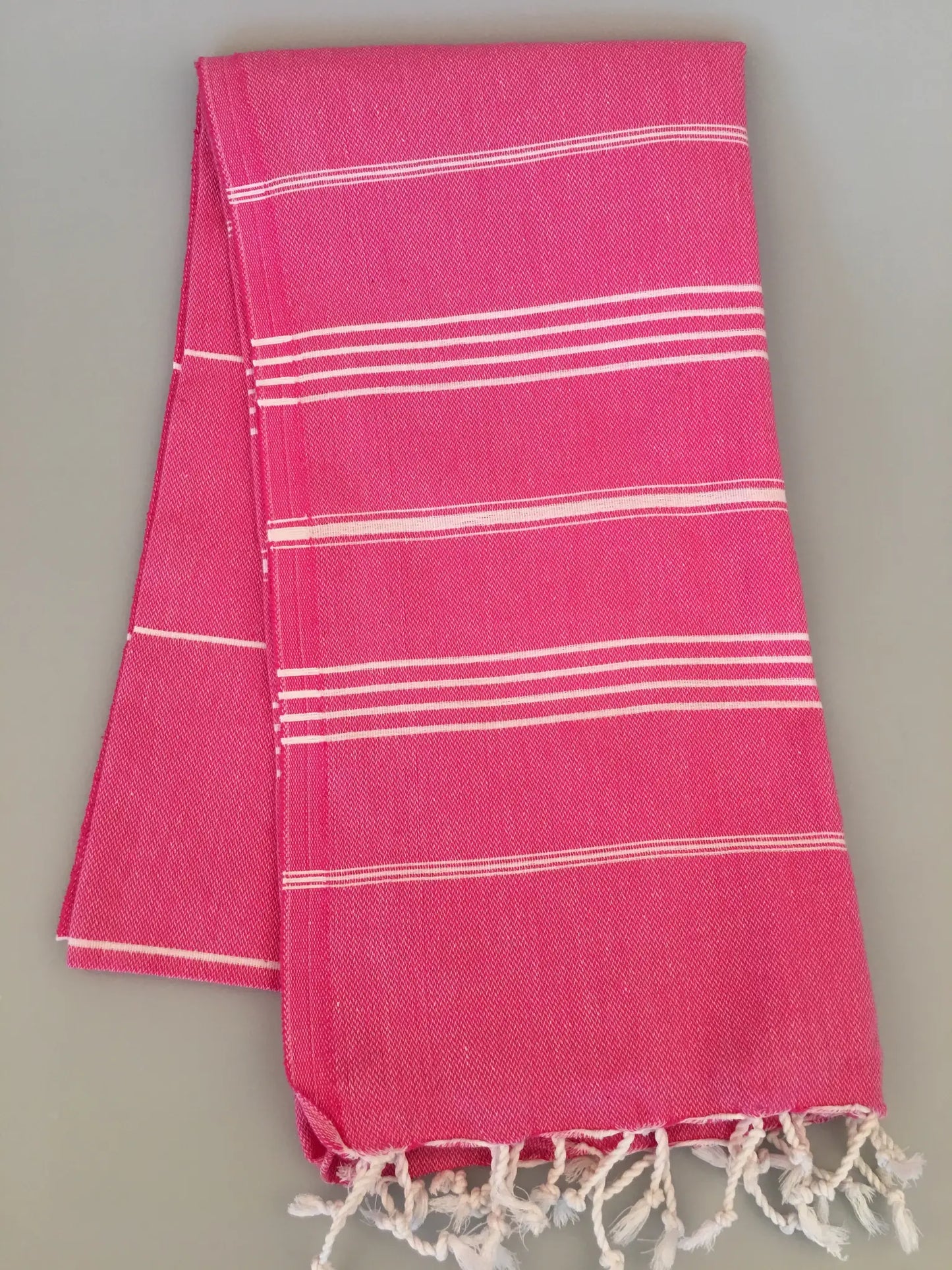 "Bright pink Turkish towel with white stripe patterns and fringed edges, neatly folded."