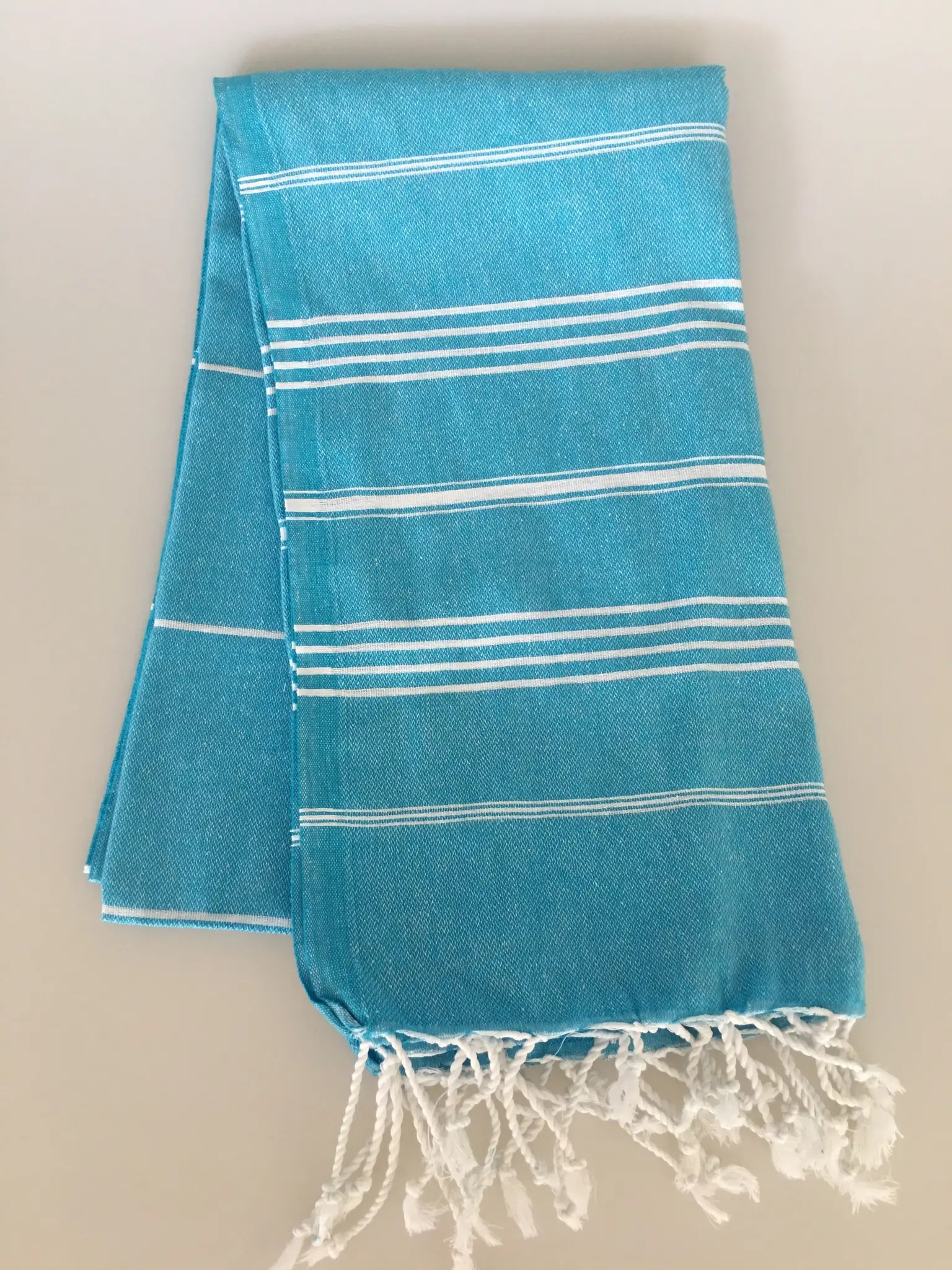 Aphrodisias Sultan Turkish towel peshtemal in vibrant turquoise with white stripes and fringed edges, folded neatly.
