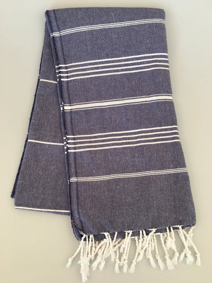 "Dark blue Turkish towel with white stripes and fringed edges, neatly folded on a light background."