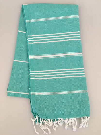 Turquoise Turkish towel with white stripes and fringed ends, laid flat on a light gray background.