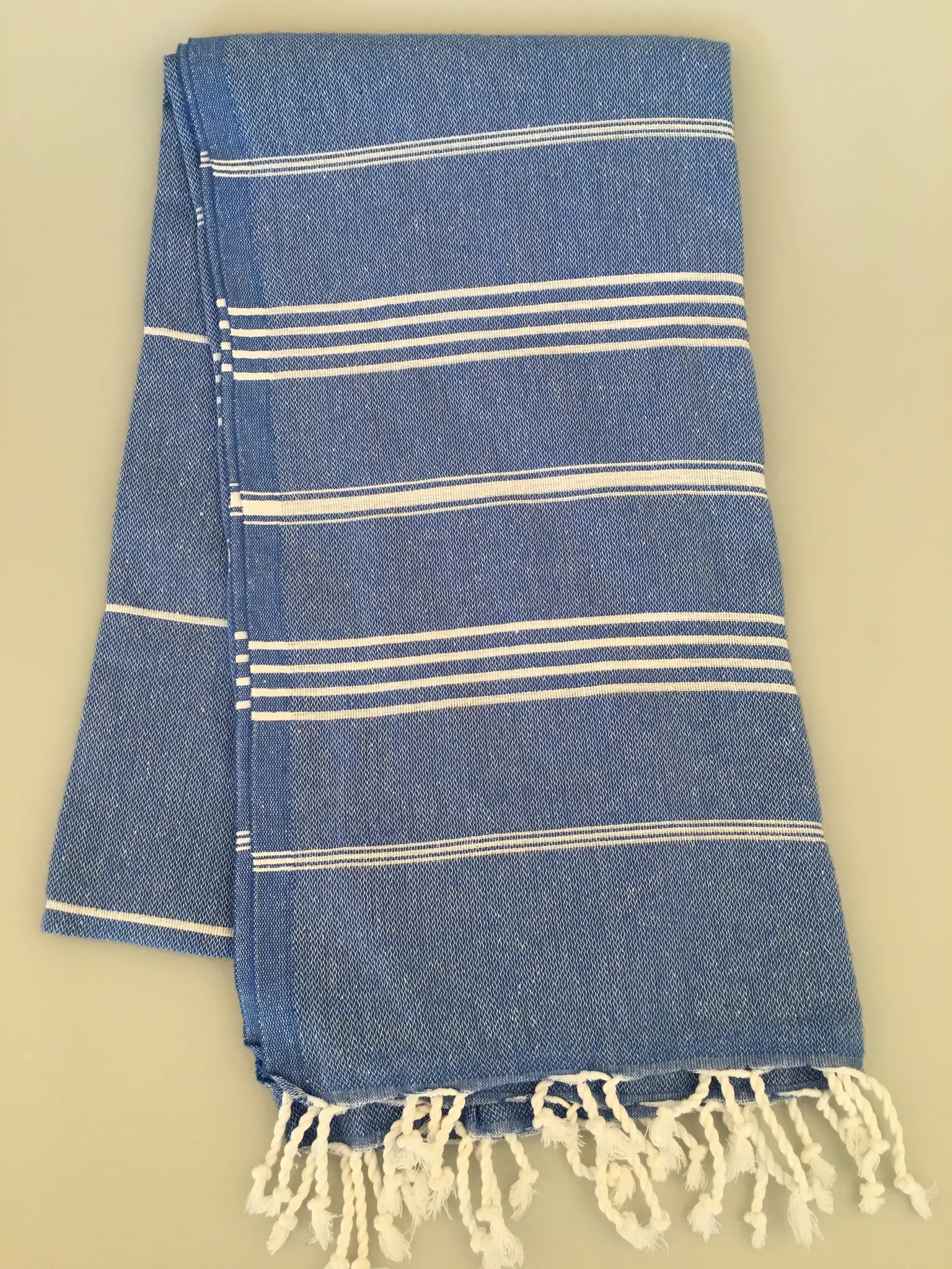 Blue and white striped Turkish towel with fringed ends, folded neatly on a light background.