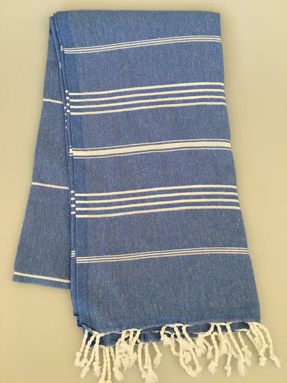 Blue and white striped Turkish towel with fringed ends, folded neatly on a light background.