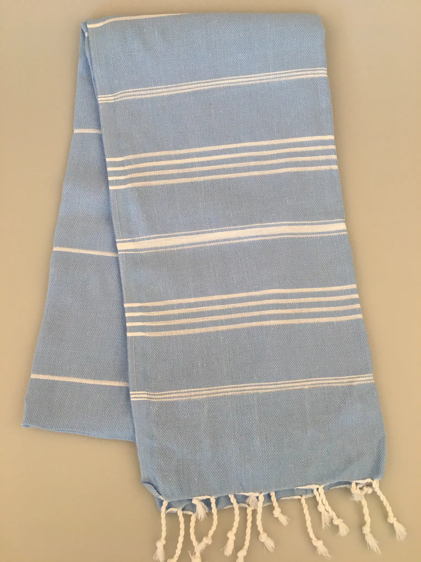 Light blue Turkish towel with white stripes and fringed edges, folded flat against a neutral background.