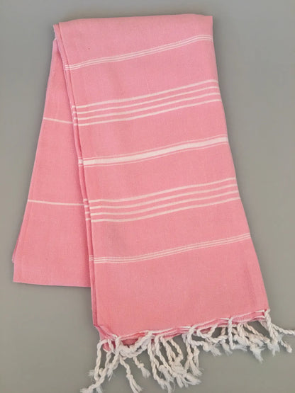 Light pink Turkish towel with white stripes and fringed edges, laid flat on a gray surface.