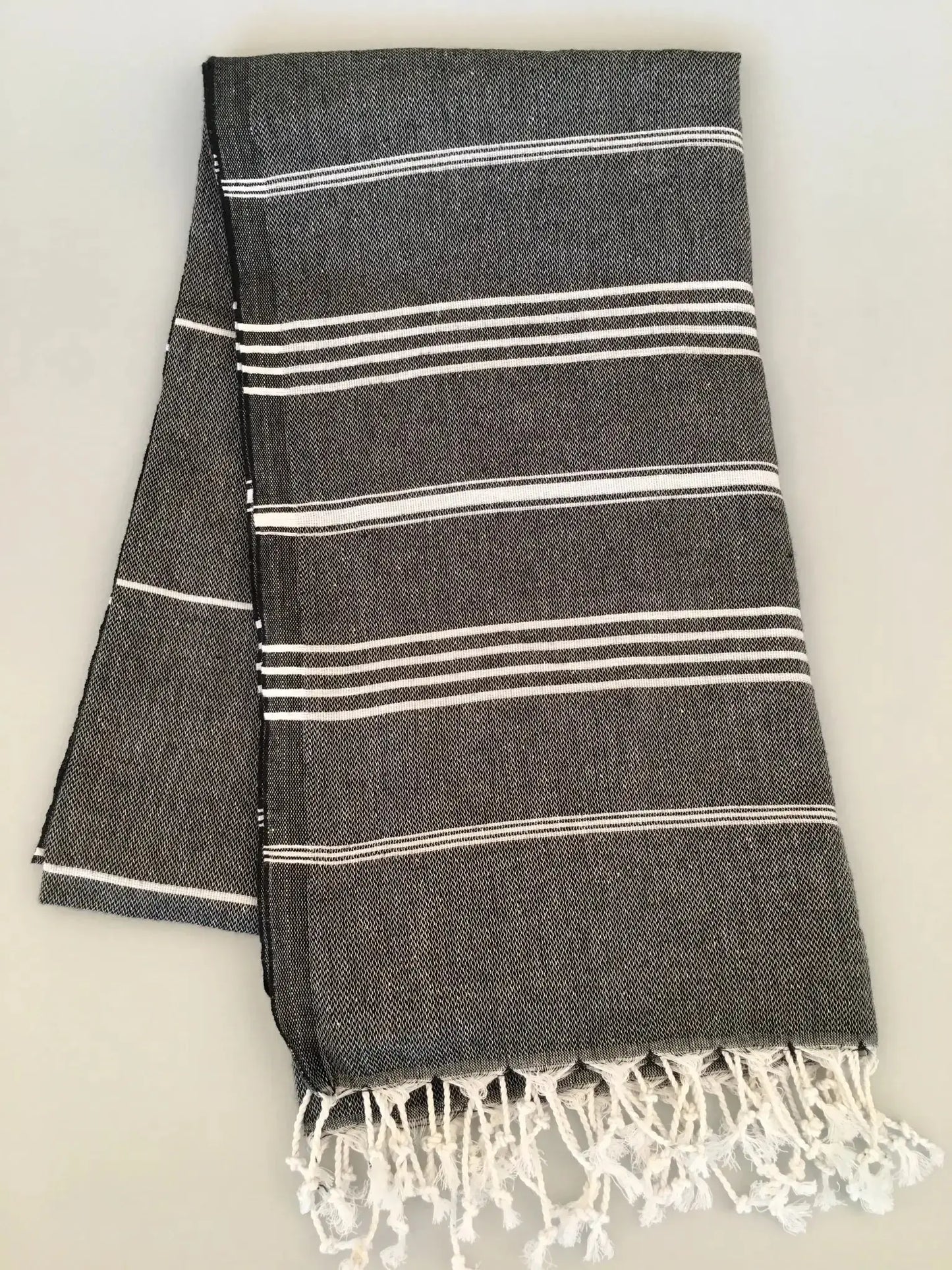 "Dark gray Turkish towel with white stripes and fringed edges, folded flat on a light background."