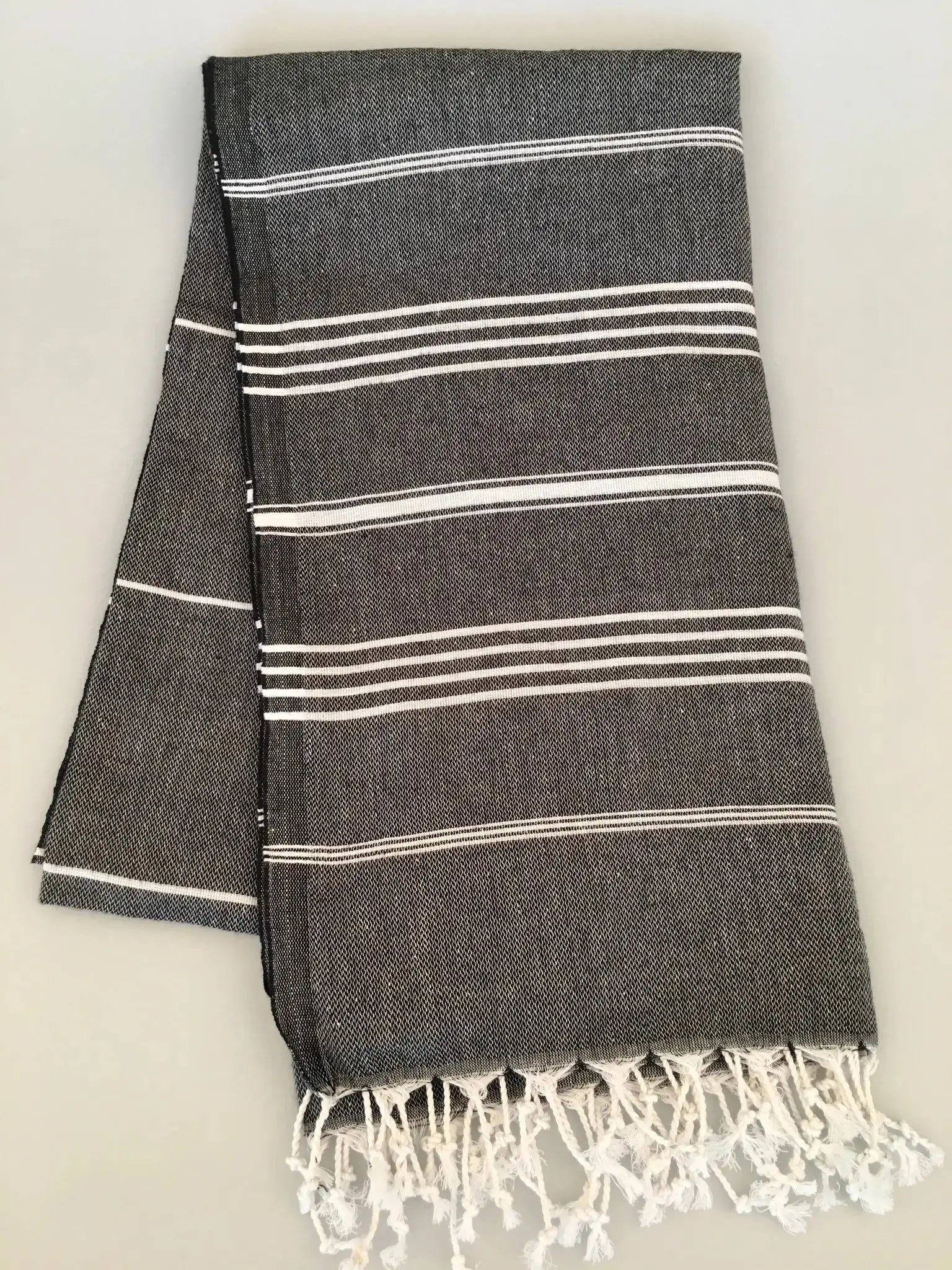 "Dark gray Turkish towel with white stripes and fringed edges, folded flat on a light background."