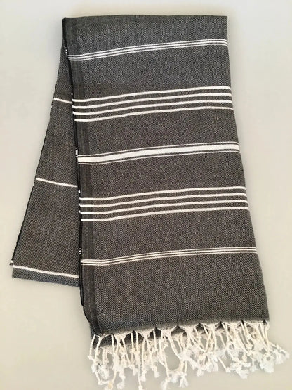 "Dark gray Turkish towel with white stripes and fringed edges, folded flat on a light background."