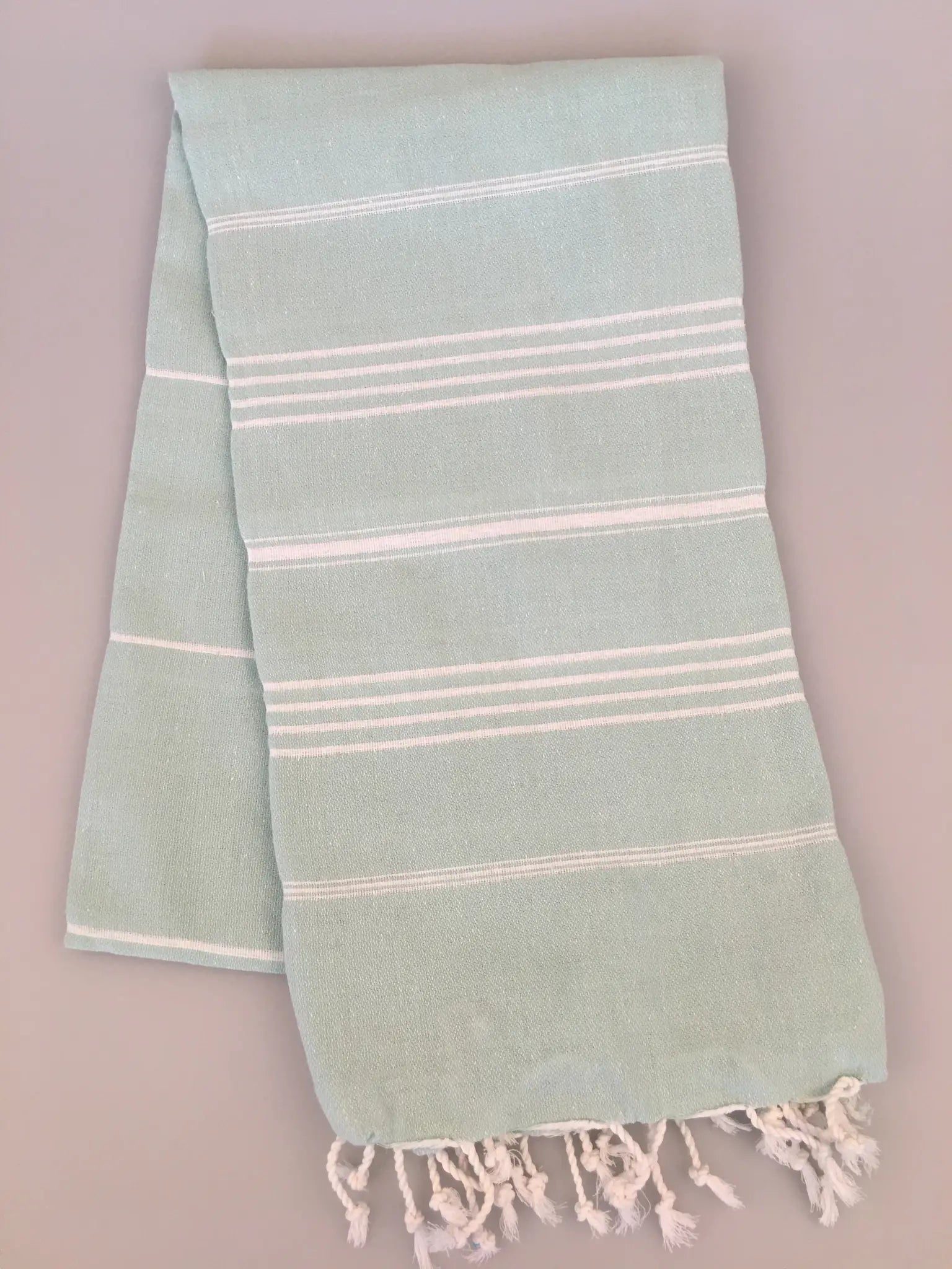 Light blue Turkish towel with white stripes and fringed edges, neatly folded.