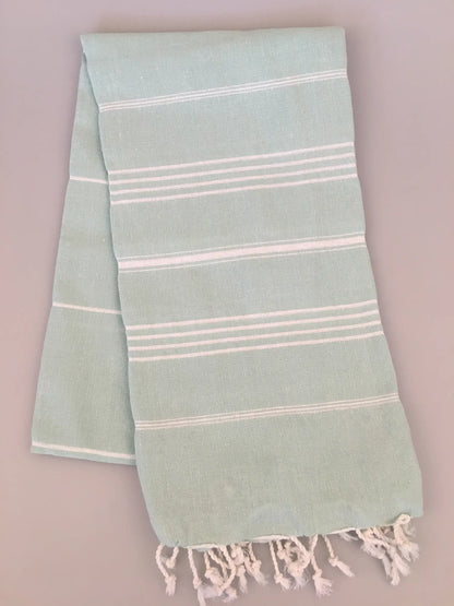 Light blue Turkish towel with white stripes and fringed edges, neatly folded.
