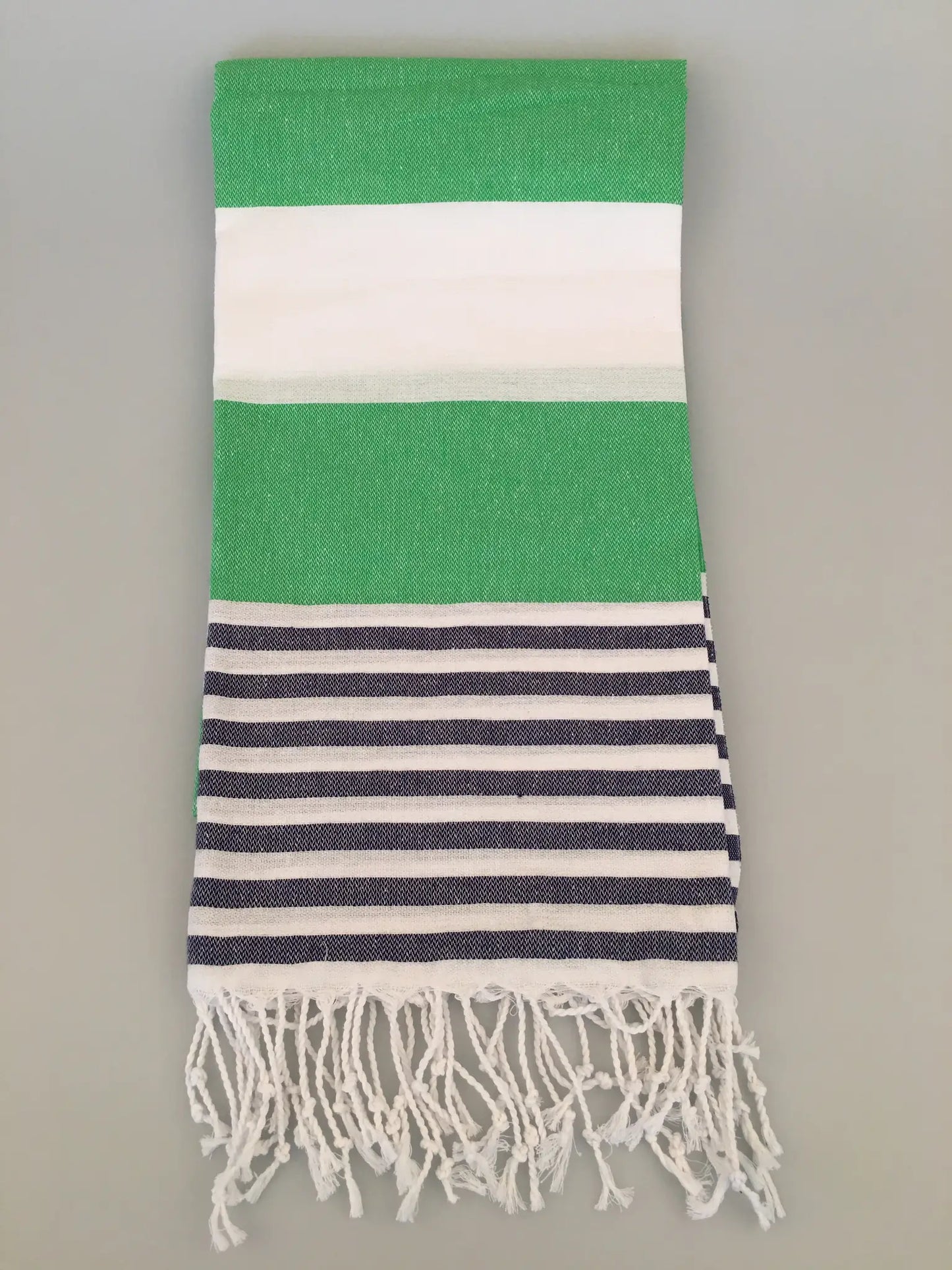 Green and white striped Turkish towel with navy blue horizontal stripes and fringed edges, laid flat on a gray background.