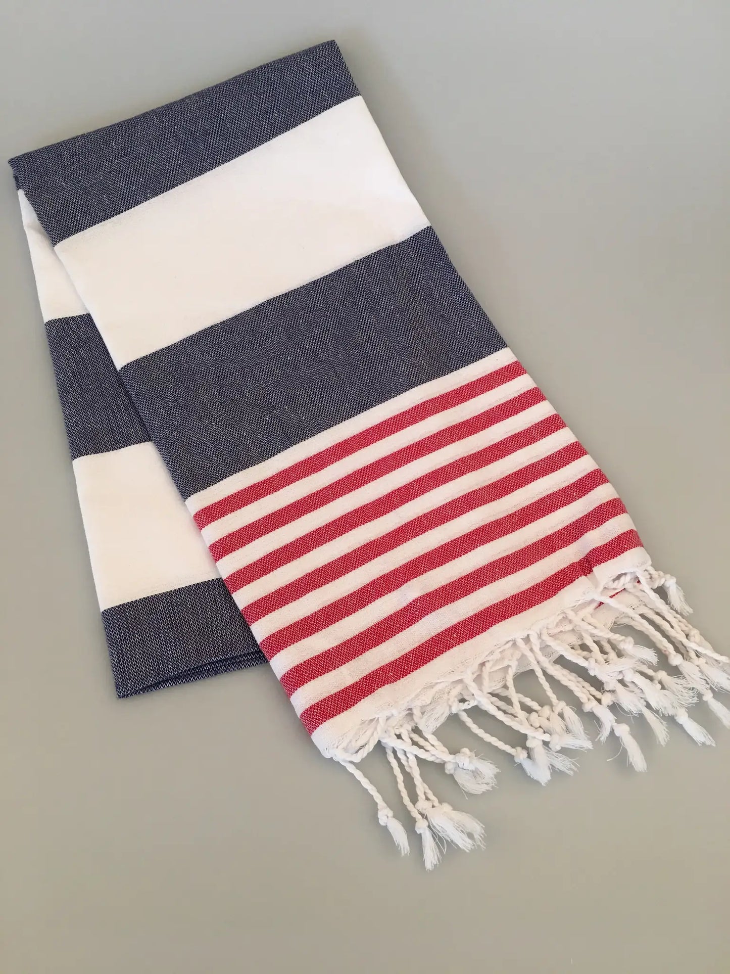 Navy blue and white striped Turkish towel with red and white striped hem and fringed ends, laid flat on a light surface.