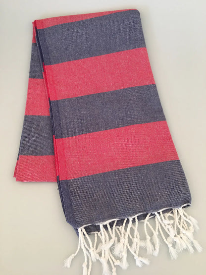 "Pinara Turkish towel peshtamal in navy blue with red stripes and white fringes, folded on a light surface."