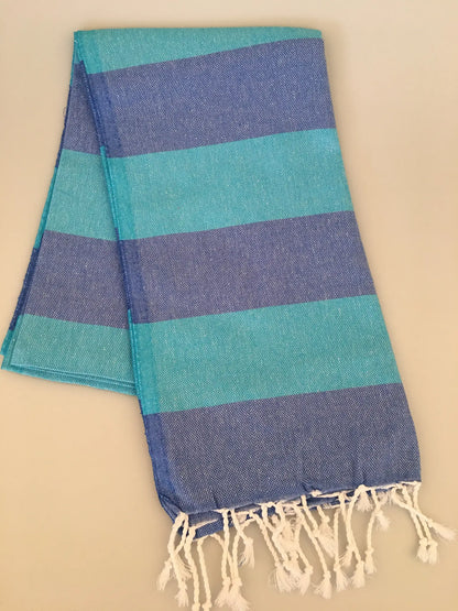 Turquoise and blue striped Turkish towel with fringed edges, laid flat on a light background.