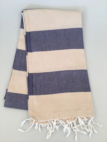 "Beige and navy striped Turkish towel with fringed edges, laid flat on a neutral background."