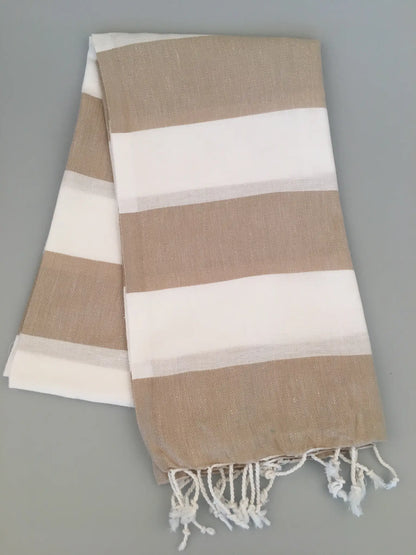 "Pinara Turkish Towel Peshtamal in beige and white stripes, folded with fringed edges, on a light gray background."