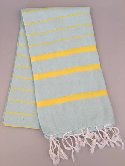 Light blue Turkish towel peshtemal with yellow stripes and white fringes, laid flat on a gray background.