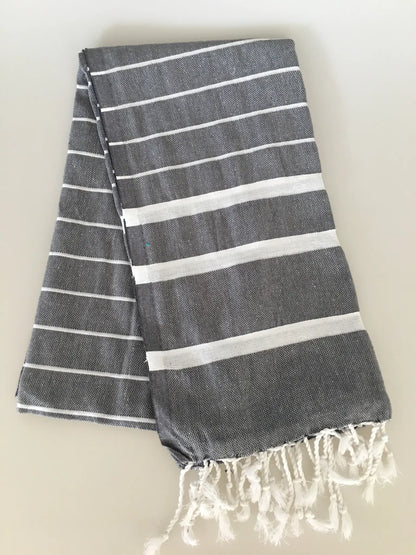 "Gray Turkish towel peshtemal with white stripes and fringed edges, neatly folded on a light background."