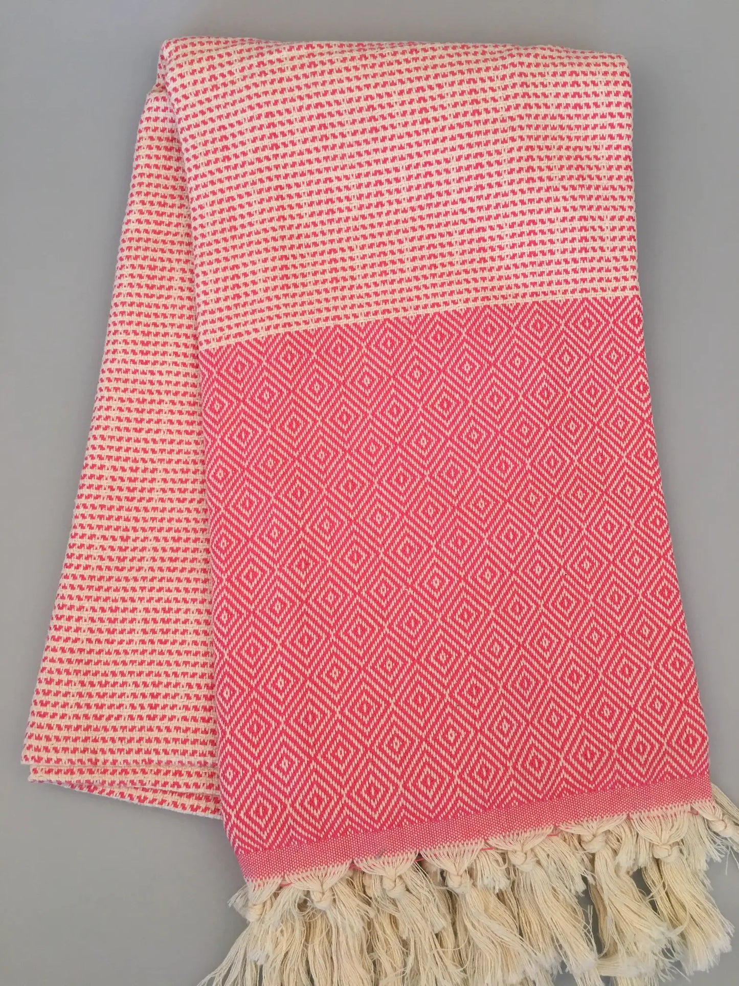 "Lycia Patara Turkish Towel in pink and white with diamond pattern and fringed edges, laid flat on a gray background."