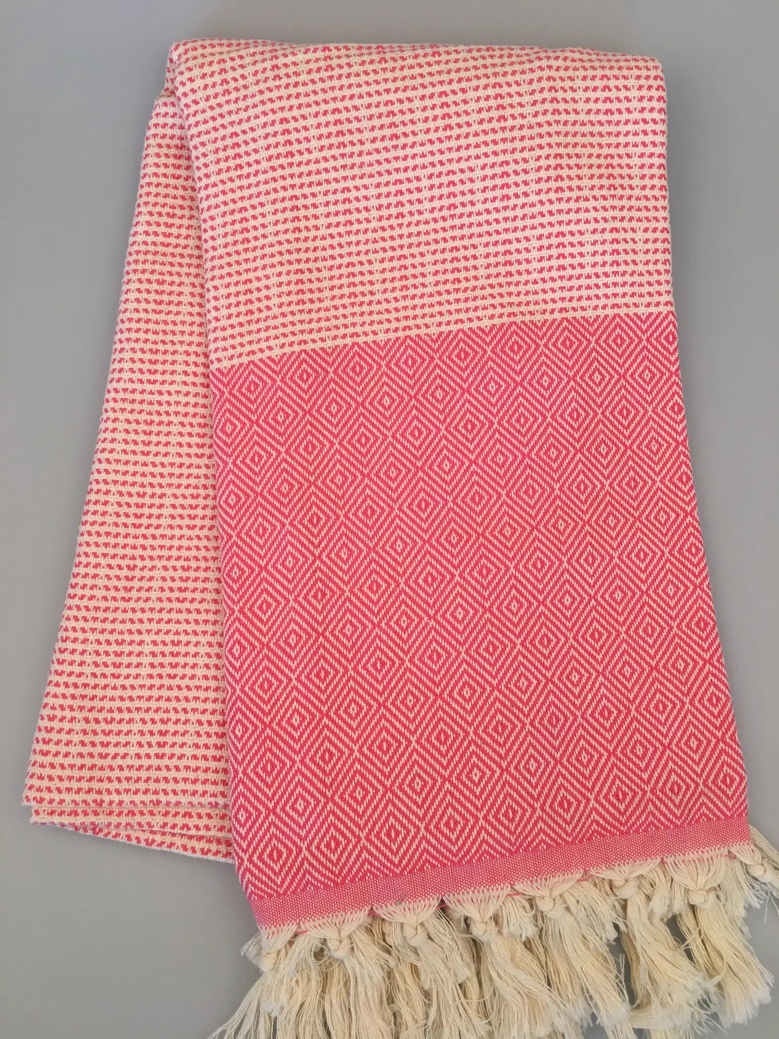 "Lycia Patara Turkish Towel in pink and white with diamond pattern and fringed edges, laid flat on a gray background."