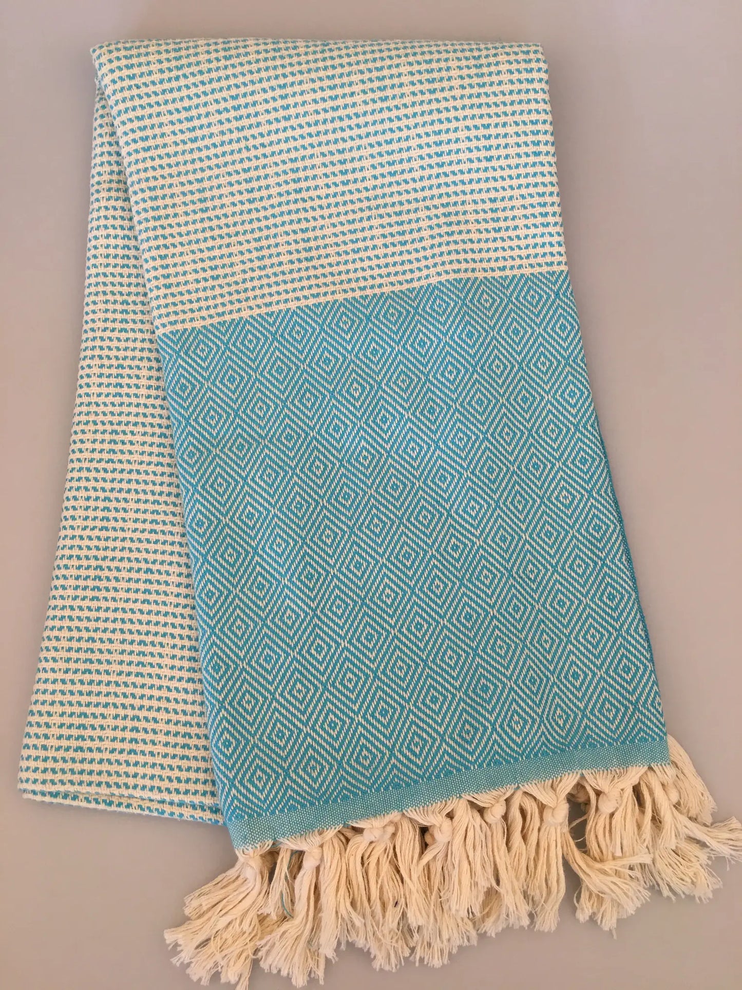 Light blue Turkish towel with diamond pattern, cream border, and fringed edges, folded on a neutral background.