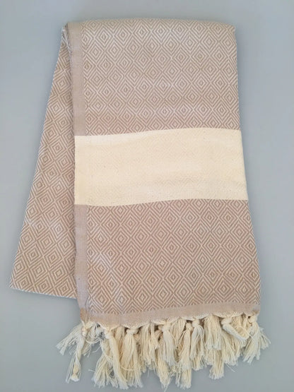 "Beige Turkish towel with diamond pattern, cream stripe, and fringed edges, laid flat on a light background."