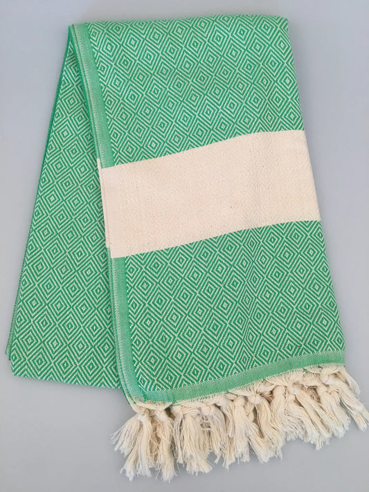 Green Turkish towel with diamond pattern, cream stripe, and fringed edges, neatly folded on a light gray background.