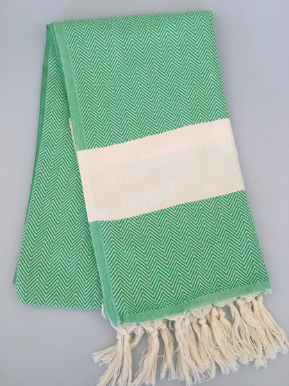 Green Turkish towel peshtemal with a herringbone pattern, featuring a white cotton band and fringed edges.