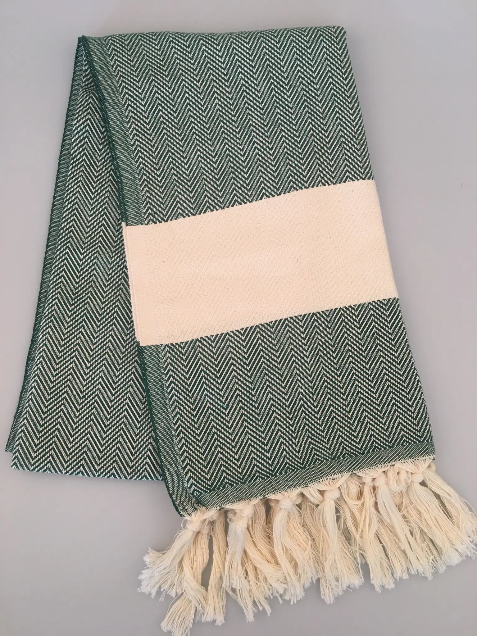 Green and white chevron-patterned Turkish towel with a cream-colored band and fringed edges, laid flat on a light background.