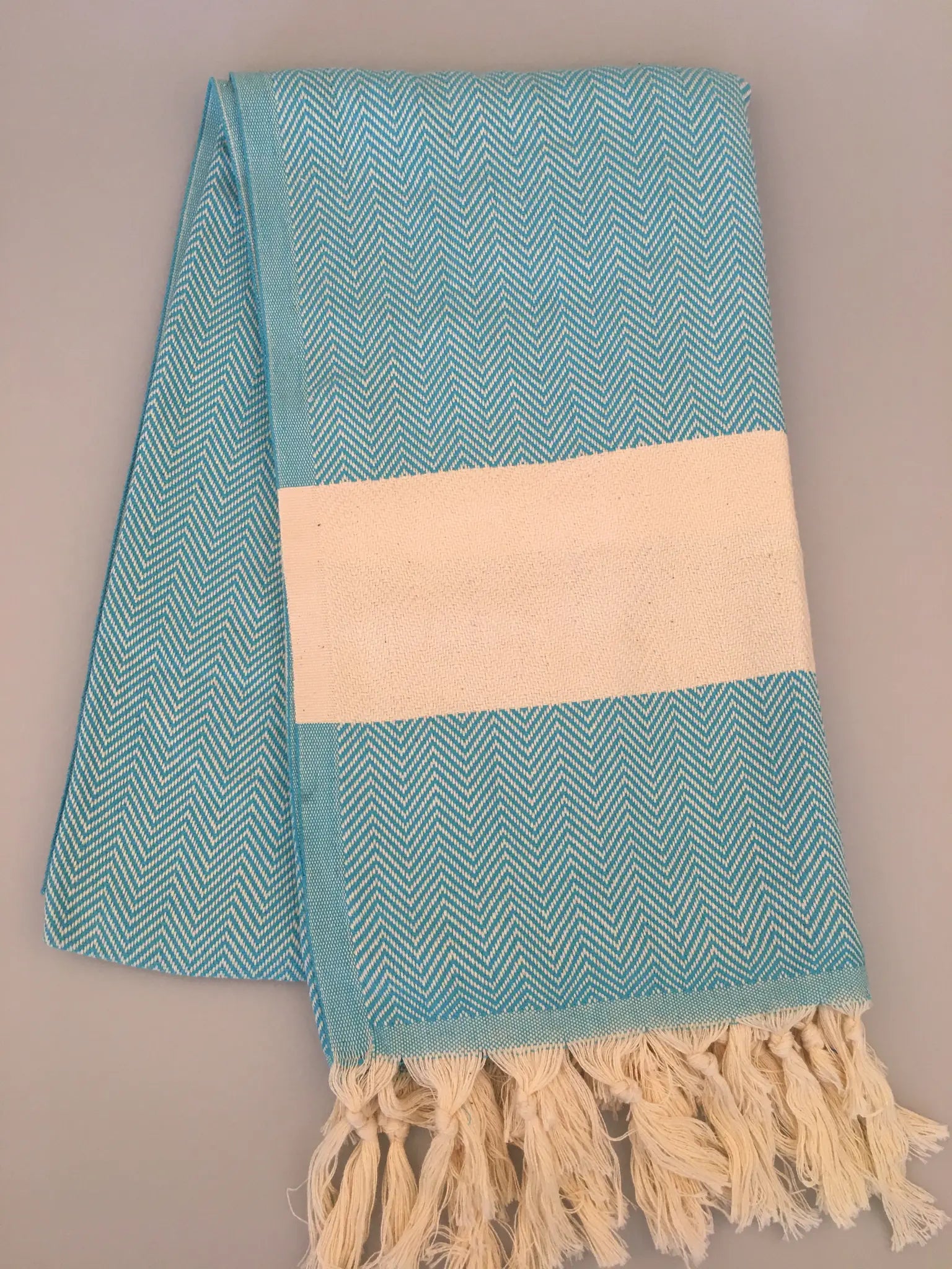 Turquoise Turkish towel peshtemal with a herringbone pattern and cream-colored stripe, fringed edges.