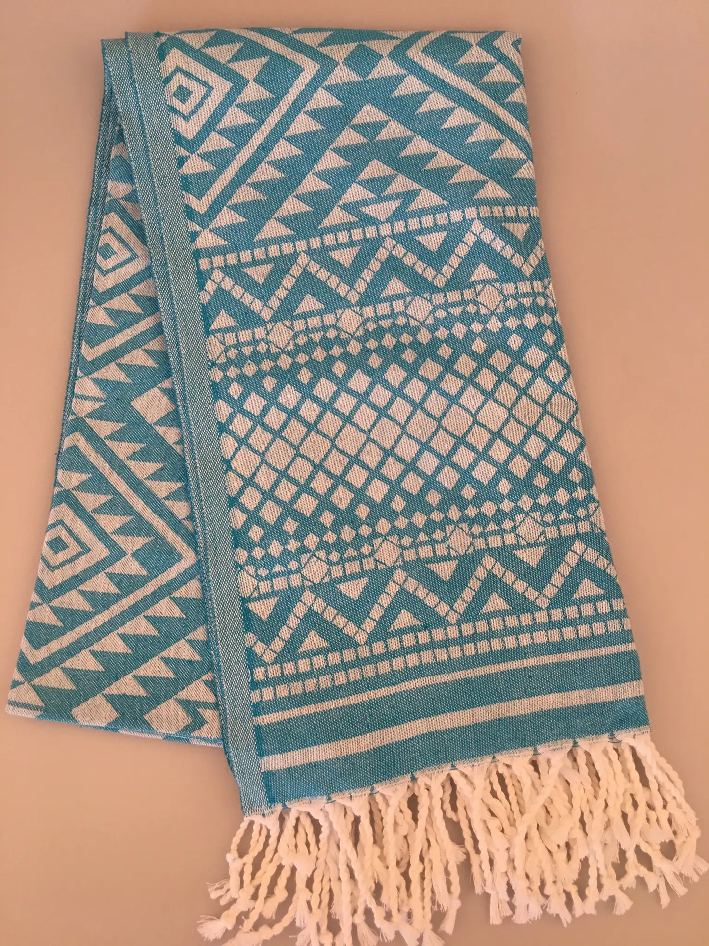Turquoise jacquard peshtemal towel with geometric patterns, featuring white fringes at one end, laid flat.