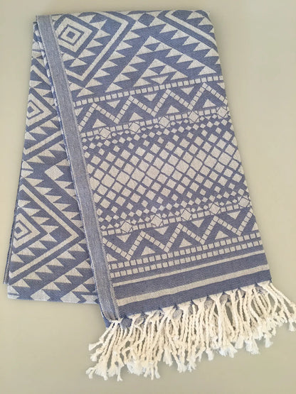 "Blue and white jacquard peshtemal towel with geometric patterns and fringed edges, folded on a light background."