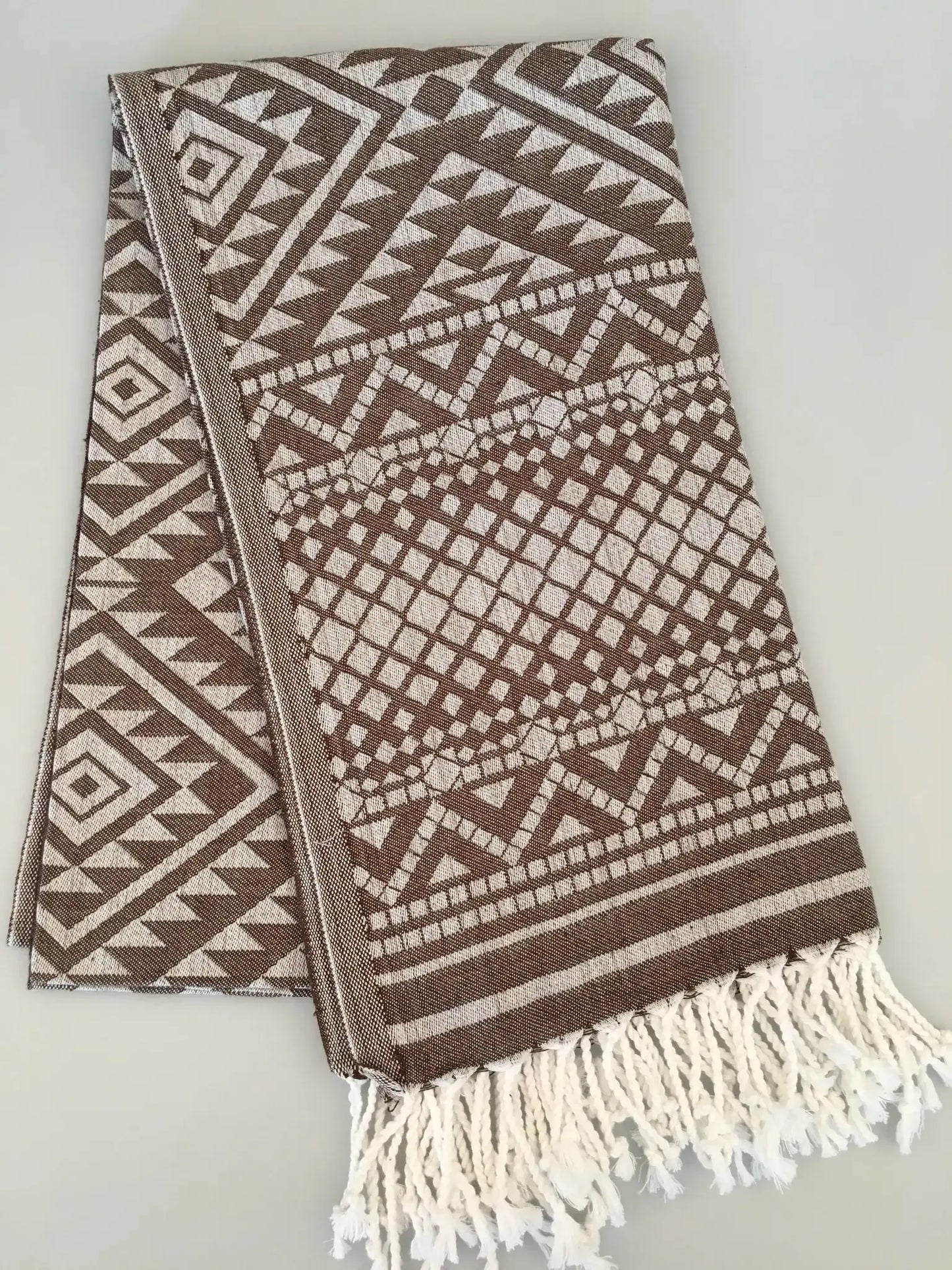 "Jacquard peshtemal in brown and cream with geometric patterns, featuring white fringes at one end."